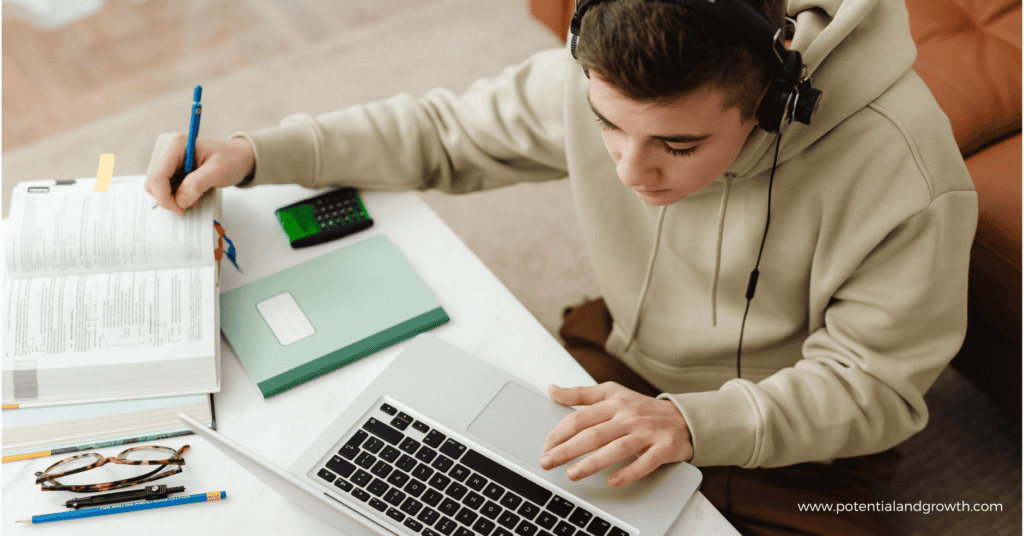 Teenage male working on computer at table with notebook beside him on the table